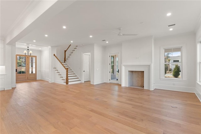 unfurnished living room with crown molding, ceiling fan with notable chandelier, and light wood-type flooring