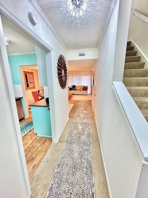 hallway featuring ornamental molding, light carpet, and a textured ceiling