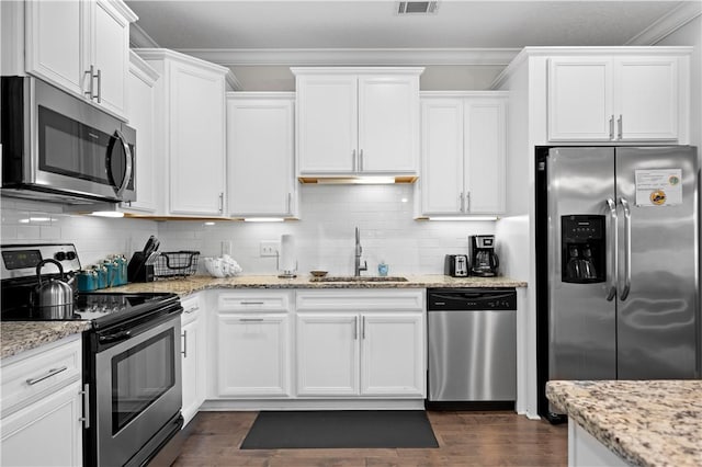 kitchen featuring appliances with stainless steel finishes, tasteful backsplash, a sink, white cabinets, and ornamental molding