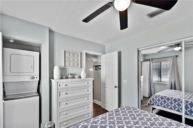 bedroom with dark wood-type flooring, stacked washer and clothes dryer, and ceiling fan