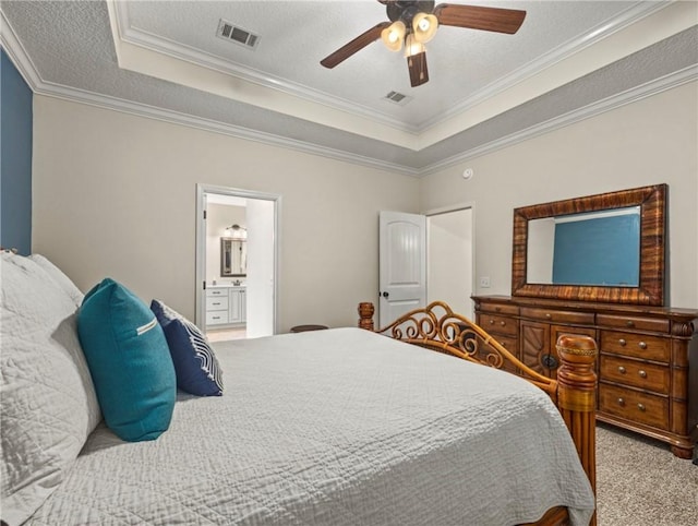 carpeted bedroom with ensuite bathroom, ornamental molding, a textured ceiling, a tray ceiling, and ceiling fan