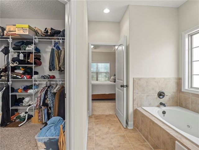 bathroom with tile patterned floors, plenty of natural light, a relaxing tiled tub, and a textured ceiling