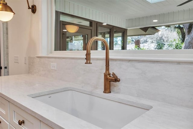 217 Five Pounds Rd, Saint Simons Island, GA 31522 - kitchen view of a sink, white cabinetry, a skylight, light stone counters, and backsplash