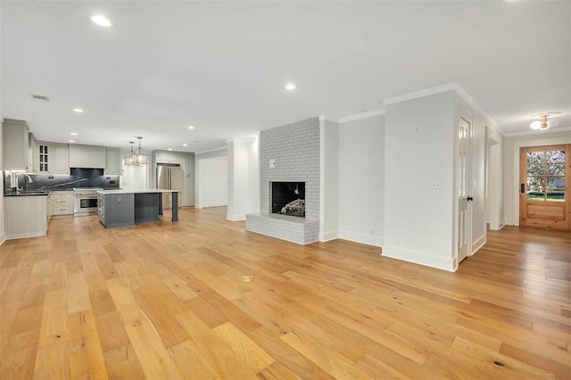 111 Youngwood Dr, Saint Simons Island, GA 31522 - unfurnished living room featuring ornamental molding, light wood-type flooring, recessed lighting, a brick fireplace, and a chandelier