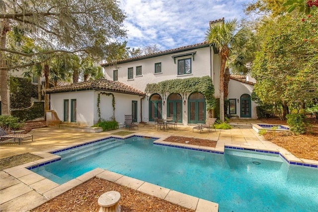 rear view of house featuring french doors, a patio, a chimney, stucco siding, and a tiled roof