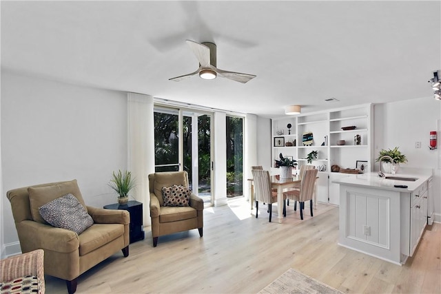 living area with ceiling fan, sink, expansive windows, and light hardwood / wood-style floors