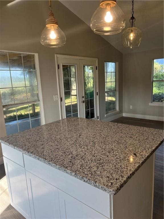 kitchen featuring lofted ceiling, light stone counters, baseboards, white cabinets, and a center island