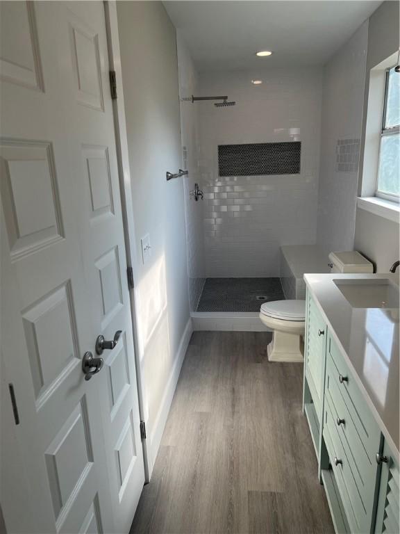 full bath featuring toilet, vanity, tiled shower, and wood finished floors