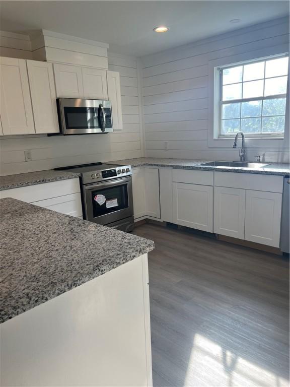 kitchen featuring white cabinets, light stone counters, dark wood-style flooring, stainless steel appliances, and a sink