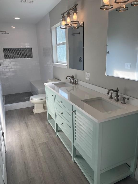 full bath with double vanity, toilet, a sink, and wood finished floors