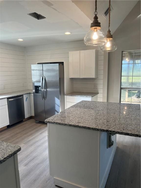 kitchen with stainless steel appliances, light wood-style flooring, white cabinets, dark stone countertops, and a kitchen bar