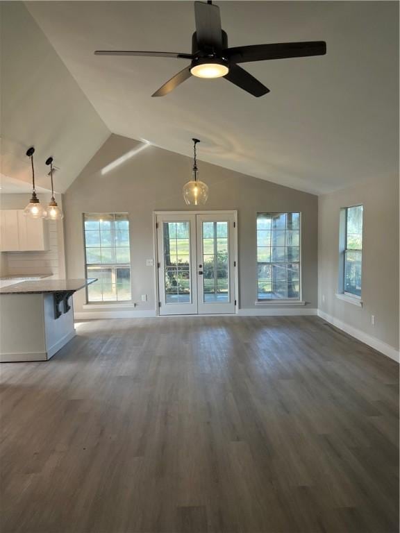 unfurnished living room with a wealth of natural light, baseboards, vaulted ceiling, and wood finished floors