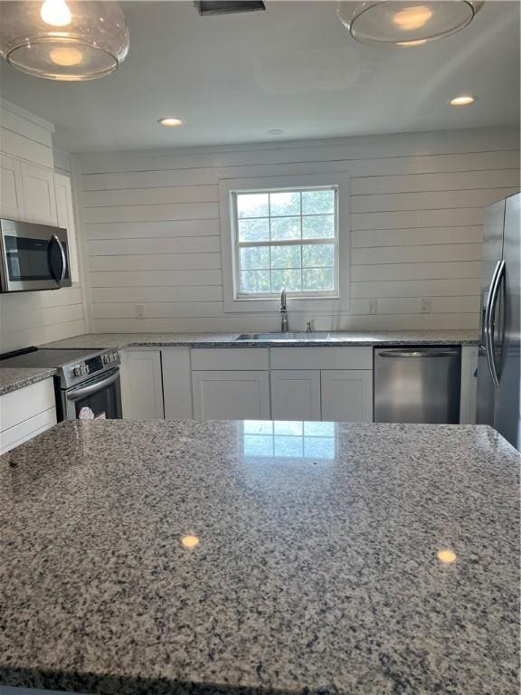 kitchen with white cabinets, light stone countertops, stainless steel appliances, and a sink