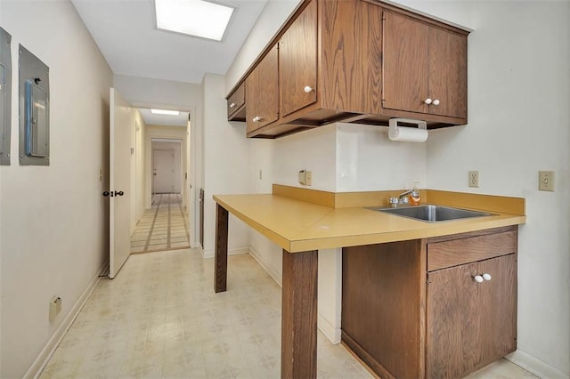 kitchen with light floors, light countertops, brown cabinetry, a sink, and electric panel