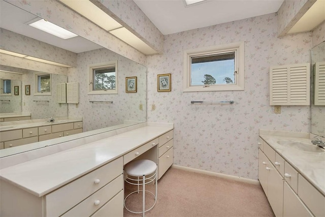 bathroom with baseboards, two vanities, a sink, and wallpapered walls