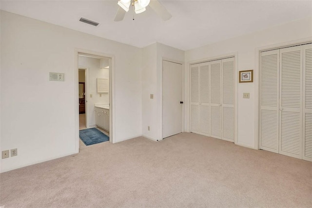 unfurnished bedroom featuring light carpet, visible vents, a ceiling fan, ensuite bath, and multiple closets