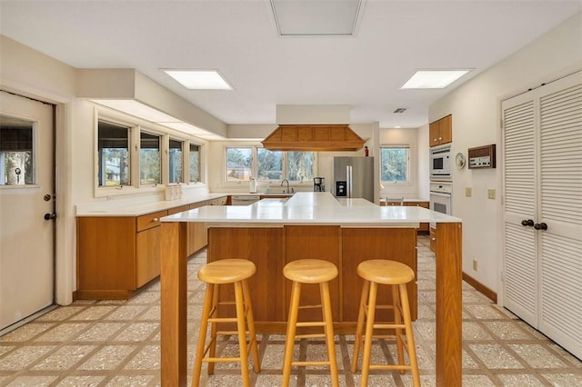 kitchen with white appliances, brown cabinetry, a sink, light countertops, and a wealth of natural light