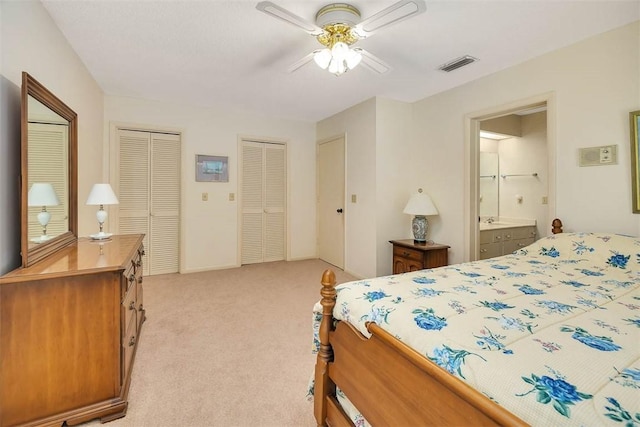 bedroom featuring light colored carpet, a ceiling fan, two closets, visible vents, and ensuite bath