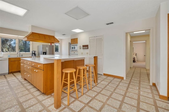 kitchen featuring light countertops, visible vents, brown cabinetry, a kitchen island, and white appliances