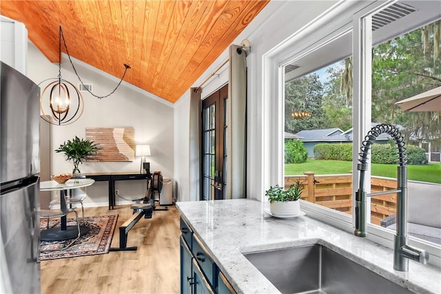 kitchen with pendant lighting, an inviting chandelier, sink, vaulted ceiling, and light wood-type flooring