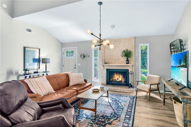 living room with a notable chandelier, a fireplace, vaulted ceiling, and hardwood / wood-style flooring