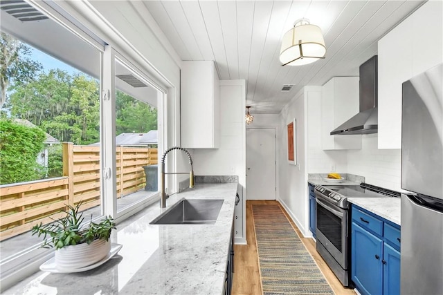 kitchen featuring white cabinetry, stainless steel appliances, wall chimney range hood, blue cabinets, and light hardwood / wood-style floors