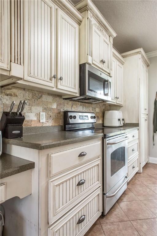 4901 Stanfield Rd, Patterson, GA 31557 - kitchen with stainless steel appliances, decorative backsplash, dark countertops, light tile patterned floors, and cream cabinets