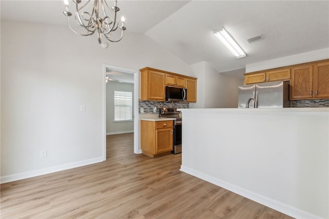 kitchen with vaulted ceiling, pendant lighting, decorative backsplash, light hardwood / wood-style floors, and stainless steel appliances