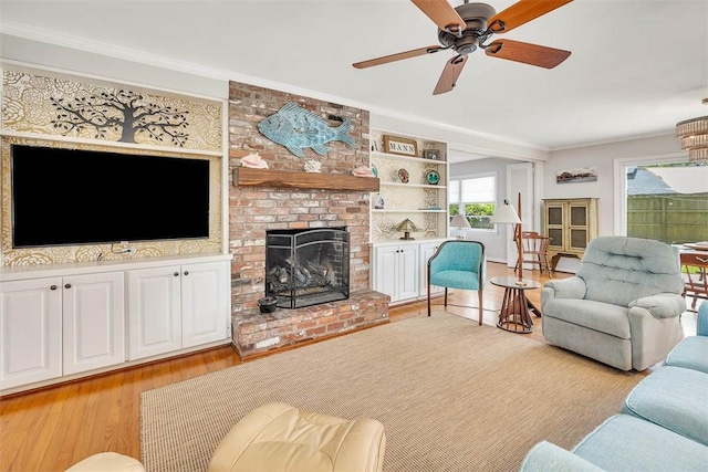 living room with a fireplace, ceiling fan, crown molding, and light wood-type flooring