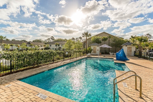 community pool with a residential view, fence, an outdoor structure, a patio area, and a shed