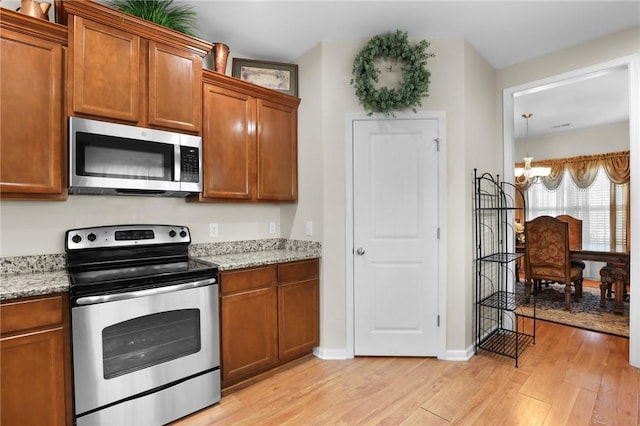 kitchen with light stone counters, appliances with stainless steel finishes, and light wood-type flooring