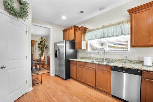 kitchen with light wood-type flooring, stainless steel appliances, light stone counters, and sink