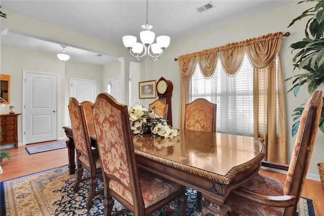 dining area with a notable chandelier, hardwood / wood-style floors, and decorative columns