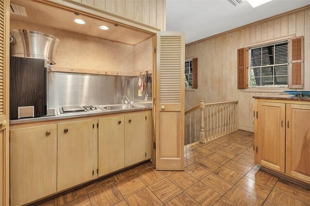 kitchen featuring light brown cabinets, wooden walls, and sink