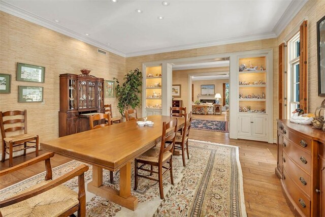 dining space with built in features, light wood-type flooring, and ornamental molding