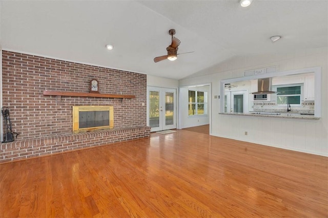 unfurnished living room featuring french doors, ceiling fan, light hardwood / wood-style floors, vaulted ceiling, and a fireplace