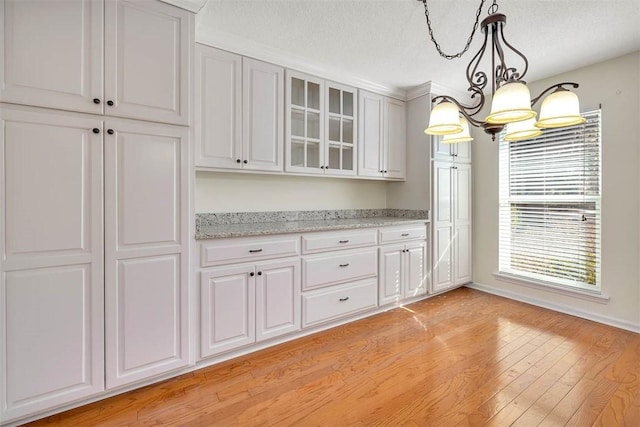 kitchen featuring hanging light fixtures, an inviting chandelier, light hardwood / wood-style floors, light stone counters, and white cabinets