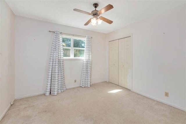 unfurnished bedroom with a closet, light colored carpet, and ceiling fan