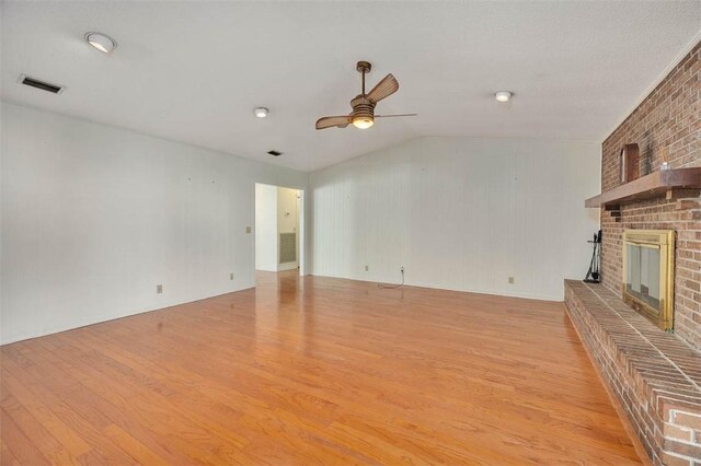 unfurnished living room featuring light wood-type flooring, lofted ceiling, a brick fireplace, and ceiling fan