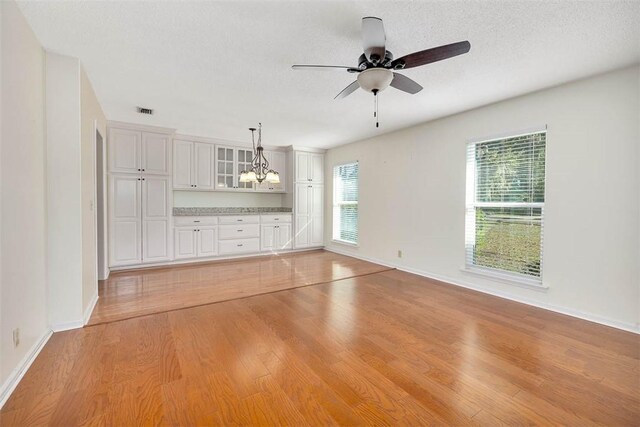 empty room with ceiling fan with notable chandelier, light hardwood / wood-style floors, and a textured ceiling