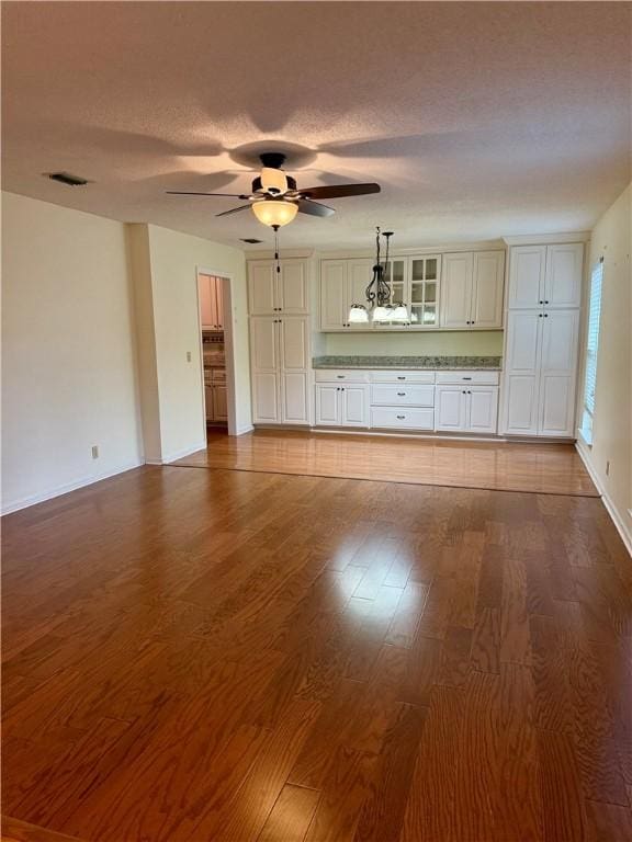 unfurnished living room featuring hardwood / wood-style flooring, ceiling fan with notable chandelier, and a textured ceiling