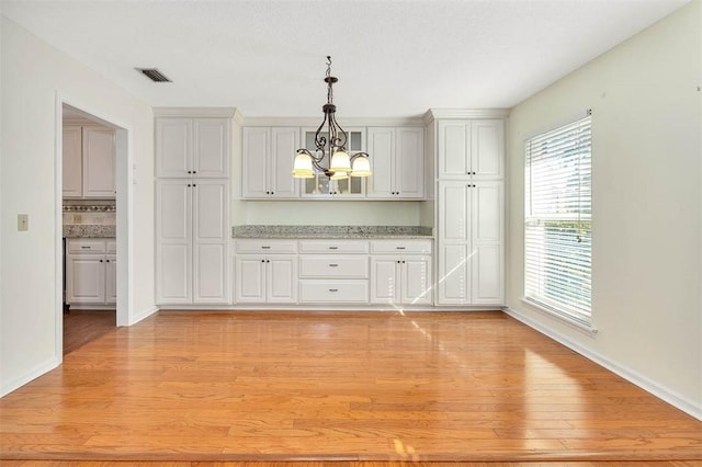 interior space featuring light wood-type flooring, decorative backsplash, hanging light fixtures, and an inviting chandelier