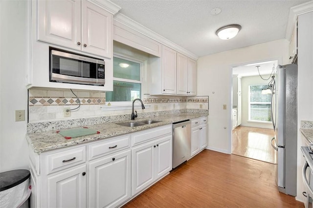 kitchen with appliances with stainless steel finishes, sink, light wood-type flooring, white cabinetry, and tasteful backsplash