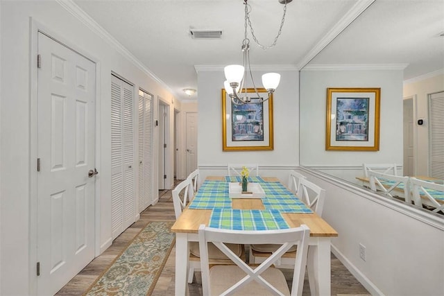 dining area featuring wood-type flooring, ornamental molding, and an inviting chandelier