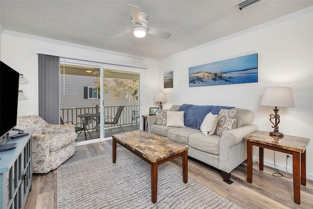 living room featuring wood-type flooring, ornamental molding, ceiling fan, and a textured ceiling