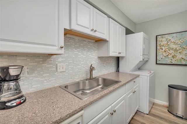 kitchen with white cabinetry, sink, backsplash, and stacked washer / drying machine