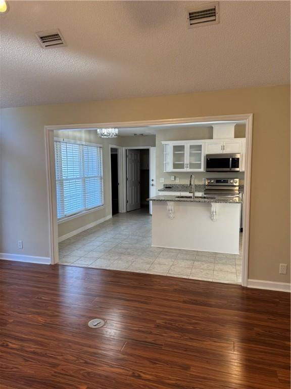 kitchen with white cabinets, light wood-type flooring, a textured ceiling, a kitchen bar, and stainless steel appliances