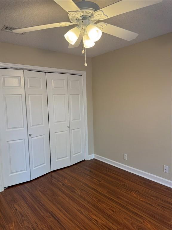 unfurnished bedroom with ceiling fan, a closet, and dark wood-type flooring