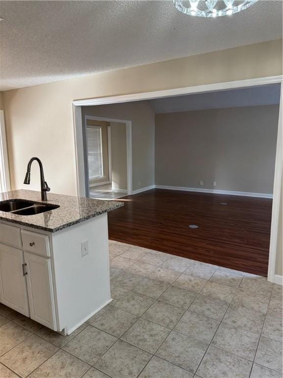 kitchen featuring light wood-type flooring, a textured ceiling, sink, stone countertops, and white cabinetry