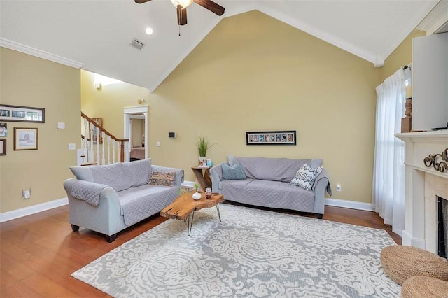 living room with ceiling fan, a premium fireplace, high vaulted ceiling, crown molding, and wood-type flooring